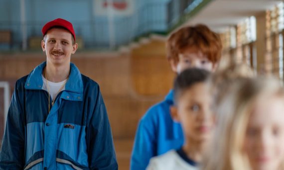 Smiling male coach guiding children in a gym setting during a physical education class.