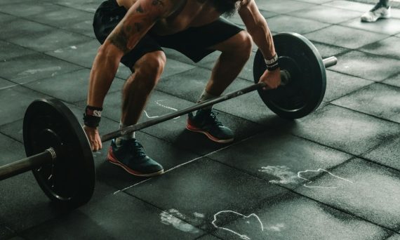 A person lifting a heavy barbell from a black rubber gym floor